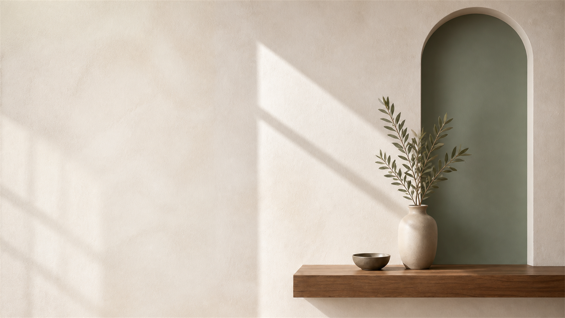 Sunlit interior corner with a sage arched niche, soft plaster wall, timber ledge and olive stems